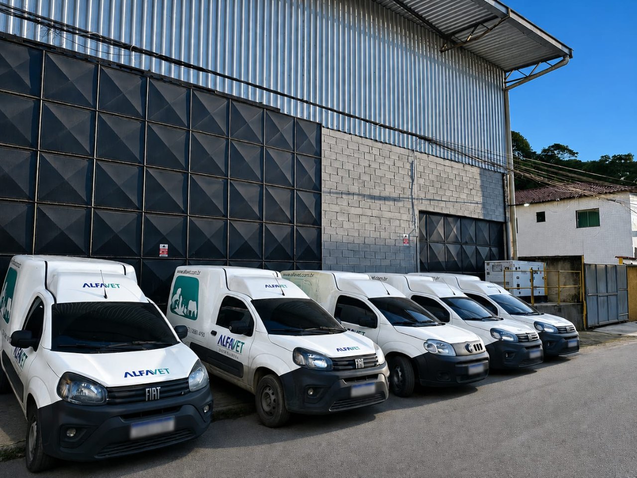 Cinco veículos da frota própria da Alfa Vet enfileirados no pátio do centro de distribuição, com a marca aplicada na lateral e no capô